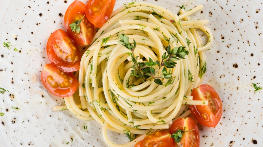Close up photo of spaghetti with sliced cherry tomatoes and herbs